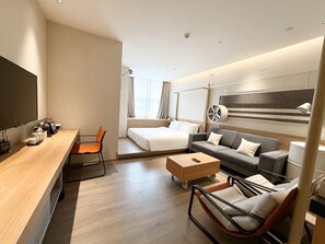 Habitación de hotel moderna con cama, sofá, mesa de centro y escritorio con silla.