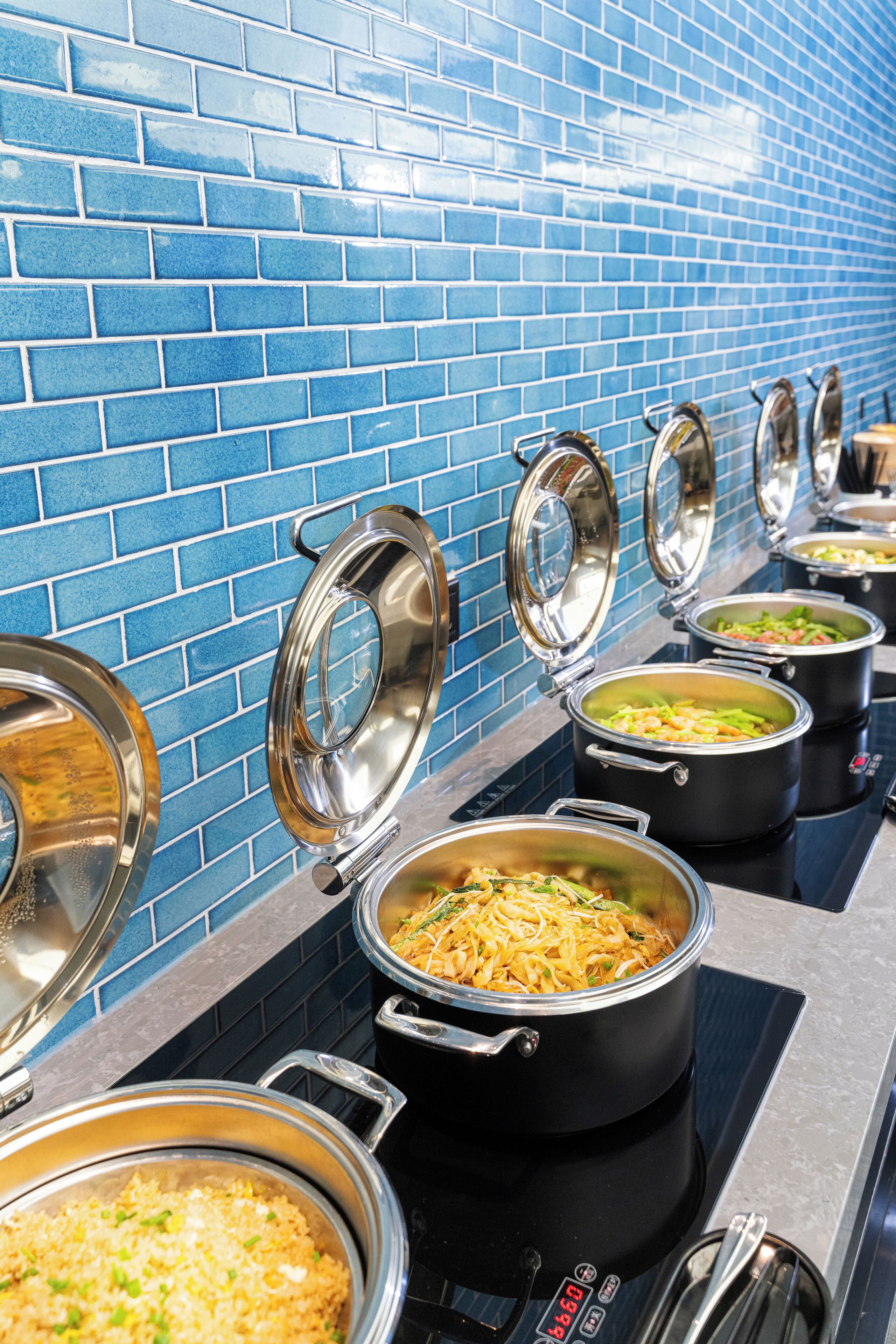 Eine Buffetlinie mit mehreren Speisenstationen, jeweils mit einem abgedeckten Topf.