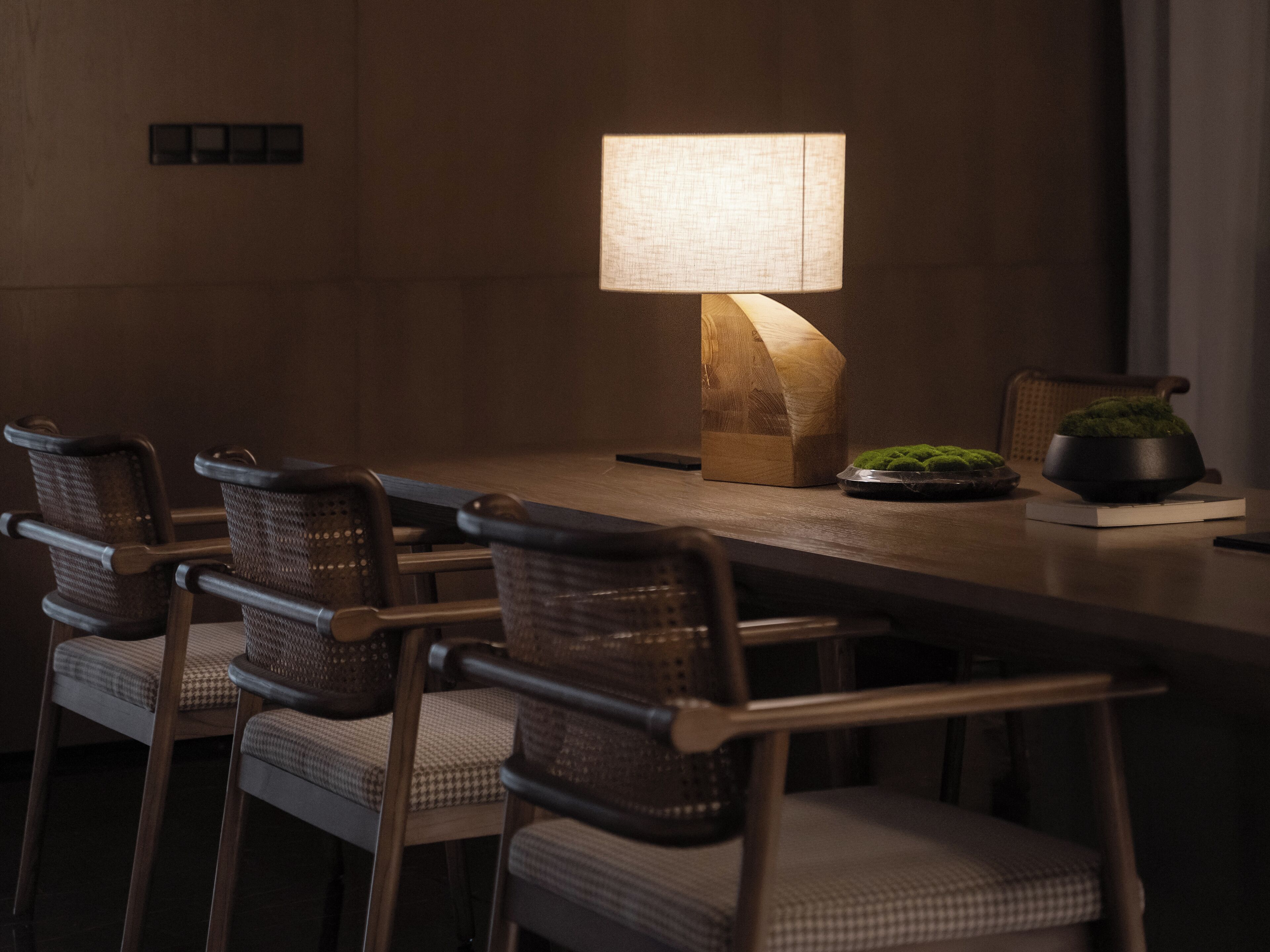 Ein Essbereich mit Holztisch, Korbstühlen, einer Lampe und einem kleinen Blumentopf.