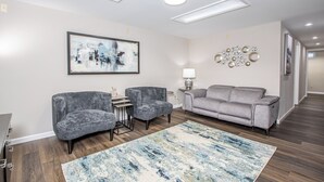 A modern living room with a gray sofa, two armchairs, a coffee table, and a large abstract painting on the wall. - Fury House • Fenton/St Louis/Lindbergh • 4BR/3BA (Fenton)
