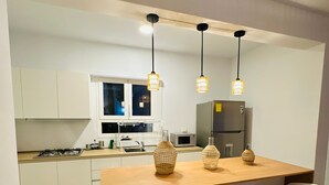 Una cocina moderna con una isla central, taburetes de bar, lámparas colgantes y un refrigerador.