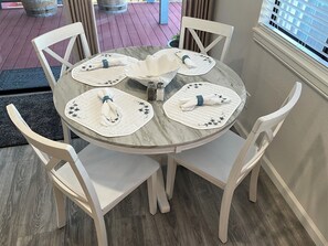 A round dining table with four white chairs, each with a placemat and napkin. - ‘The Sea Pearl” (Cayucos)