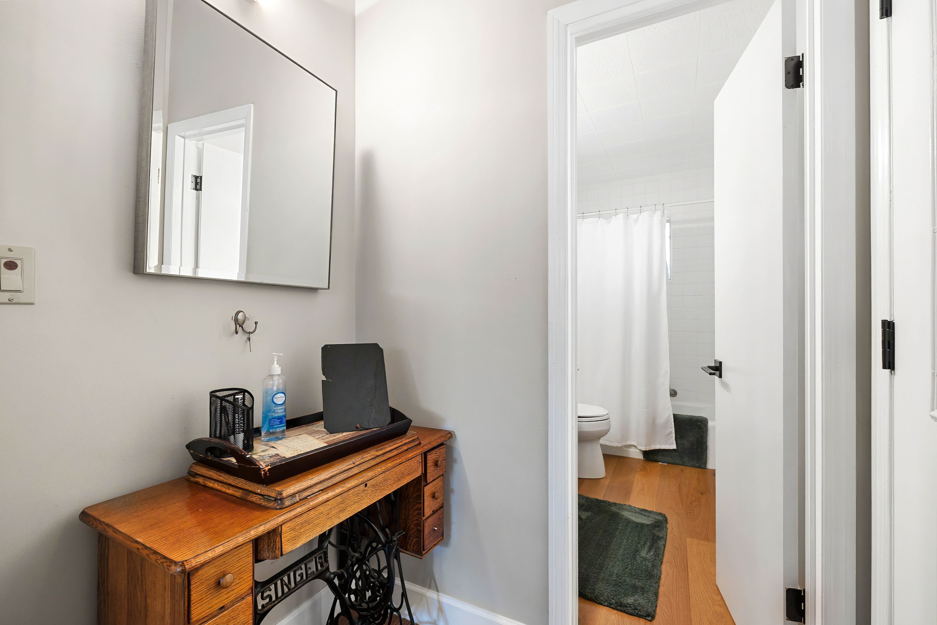 A compact bathroom with a wooden vanity, a mirror, and a shower area visible through an open door.