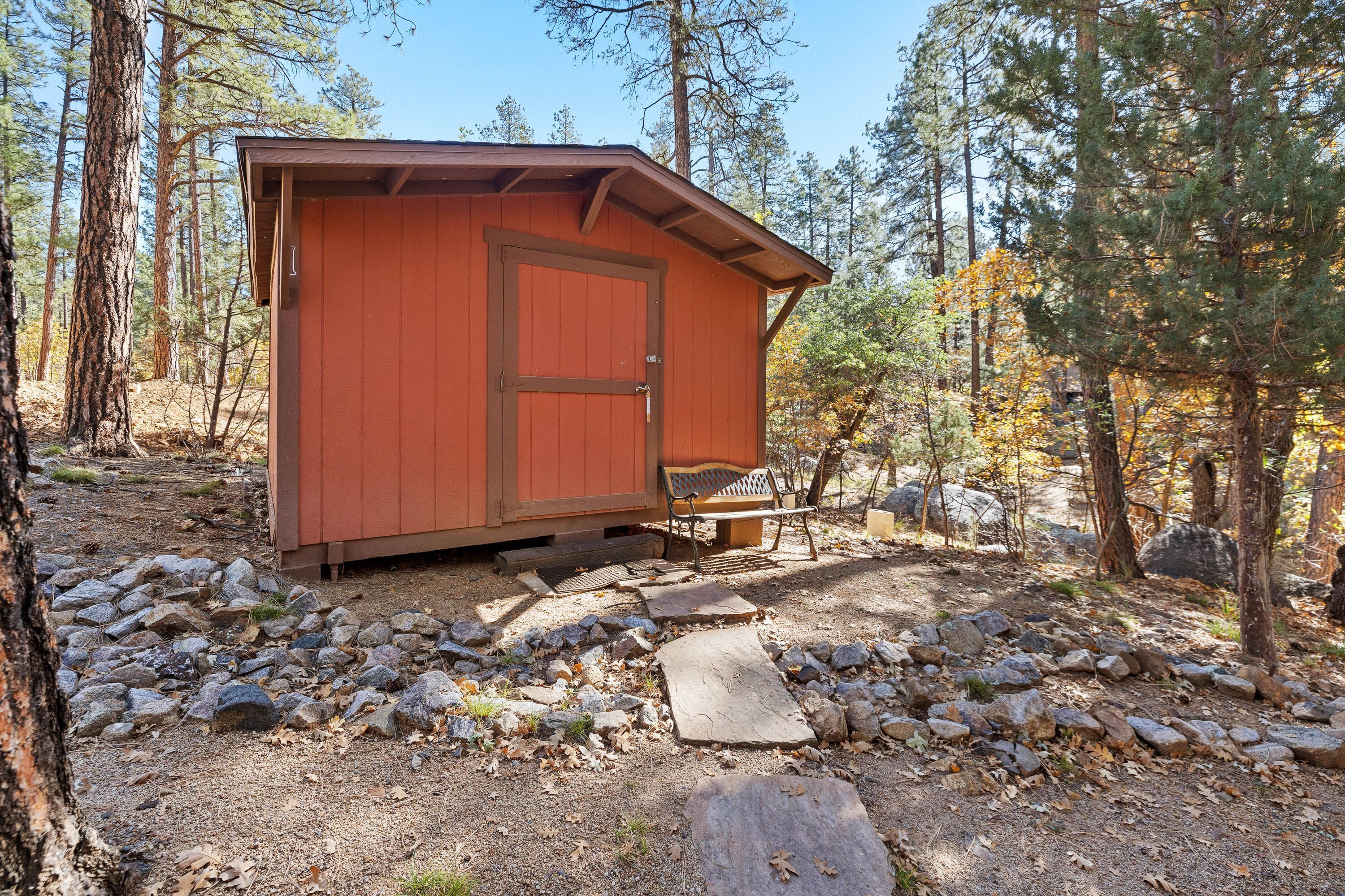 A small wooden cabin with a door and a bench outside, surrounded by trees and rocks.