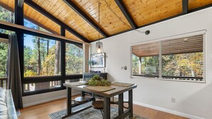 A room with a wooden ceiling, large windows, a dining table with a plant, and a sofa.