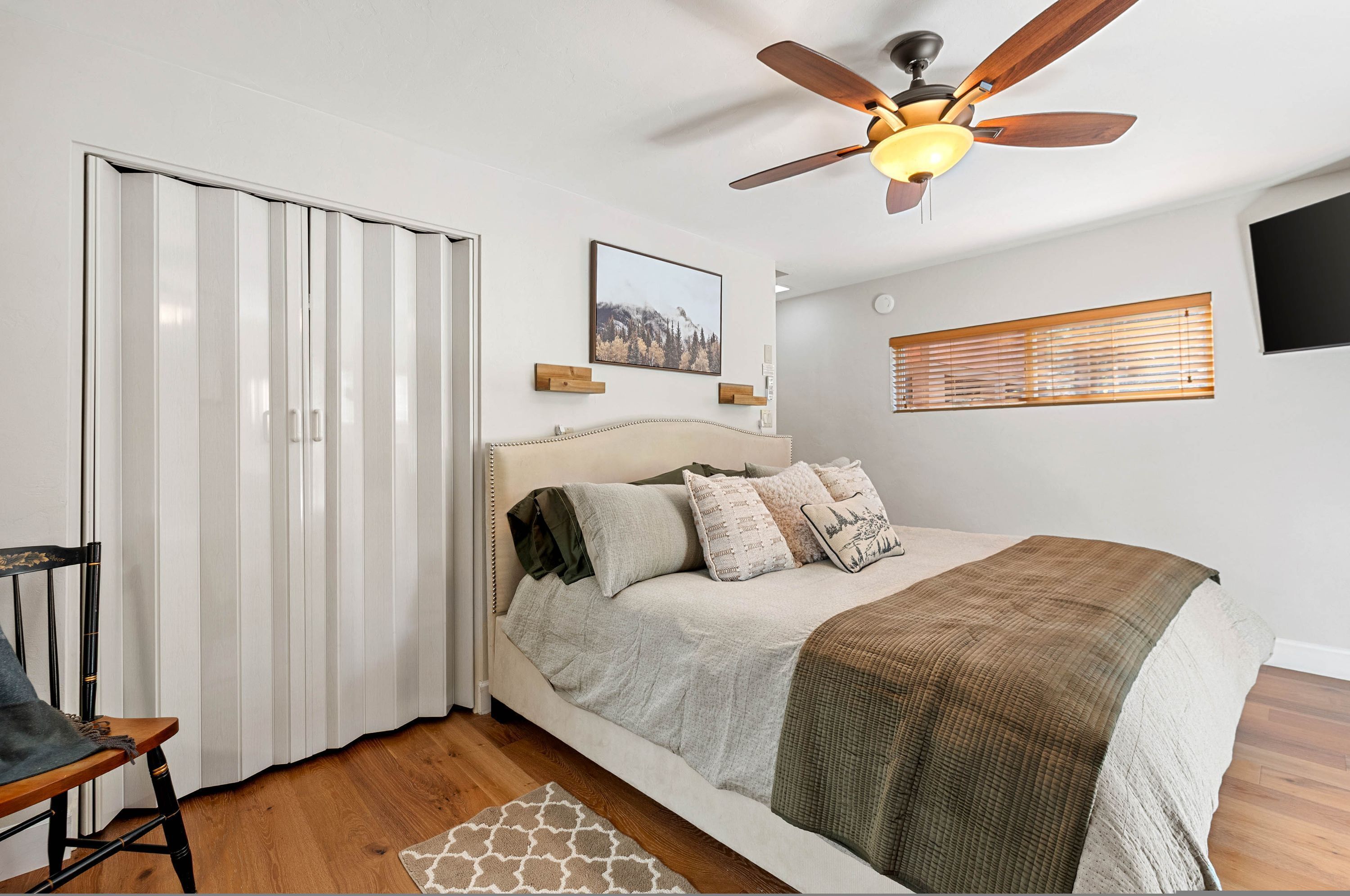 A bedroom with a bed, a ceiling fan, a window with blinds, and a door.