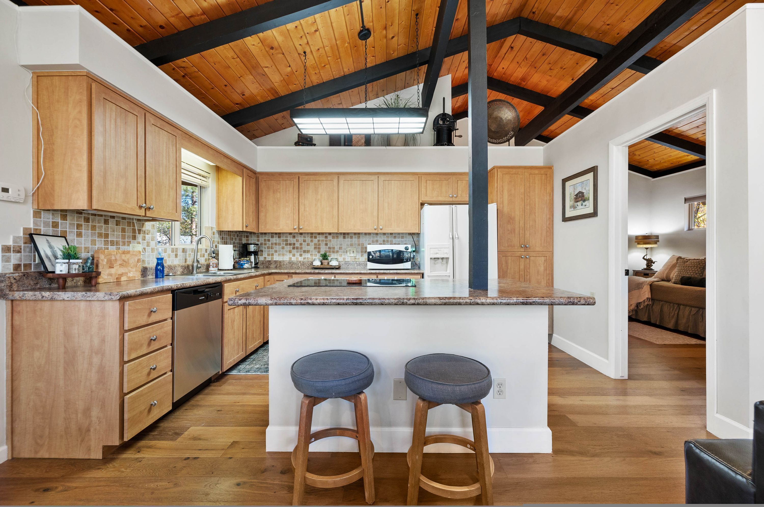A modern kitchen with wooden cabinets, a large island with stools, and a high ceiling with exposed beams.