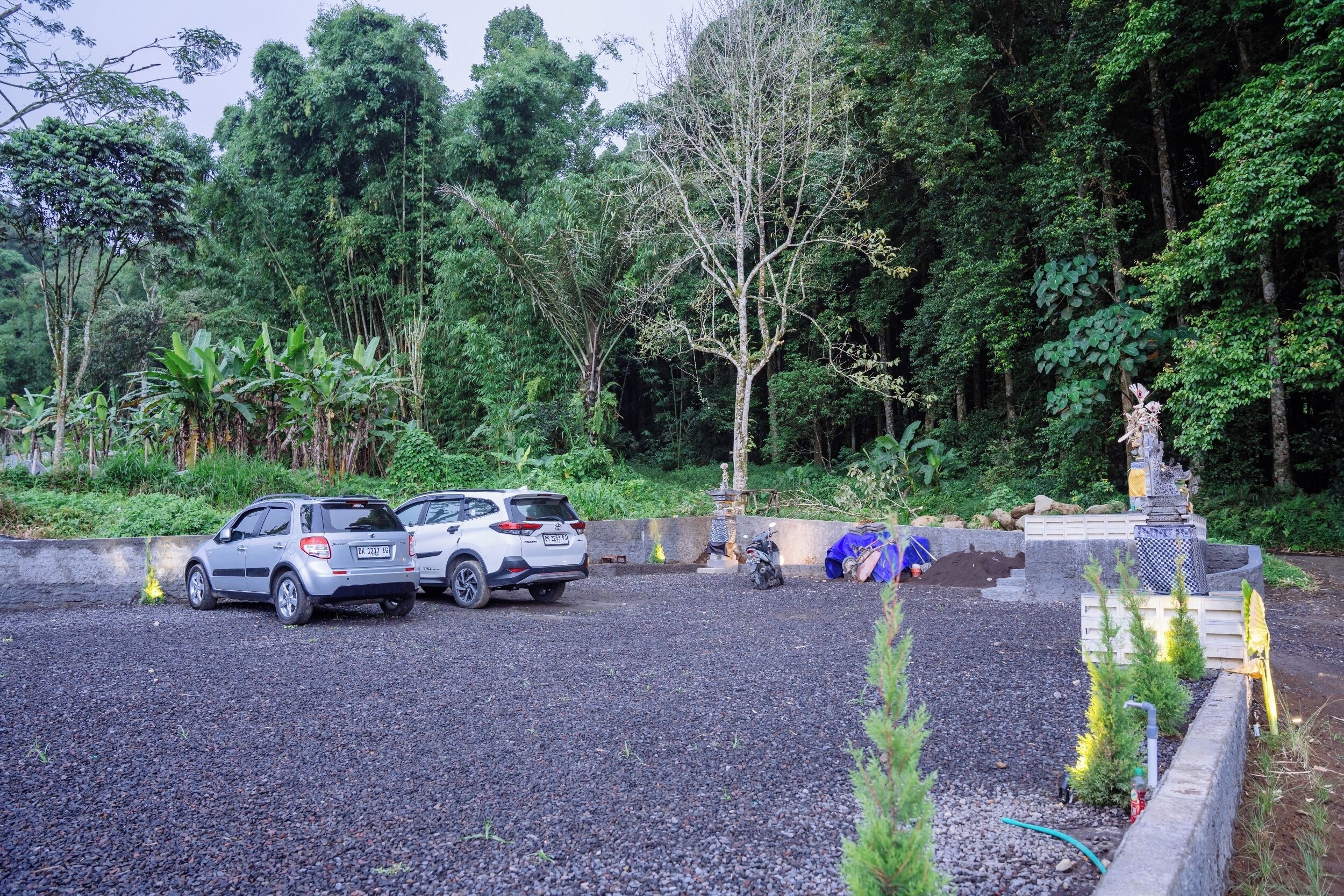 A parking area with two cars, surrounded by dense greenery and a statue.