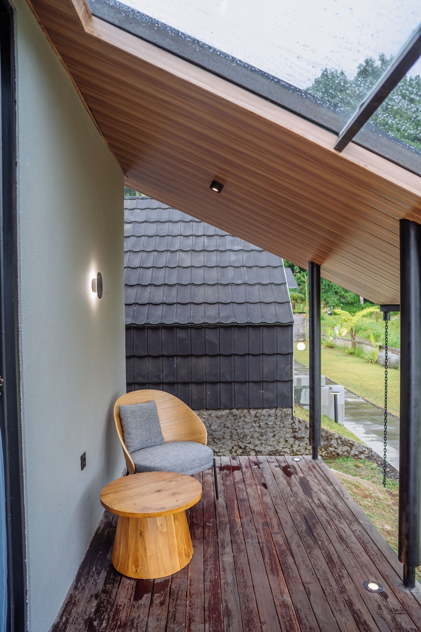 A wooden deck with a built-in bench and table, a covered area with a sloped roof, and a view of a garden.