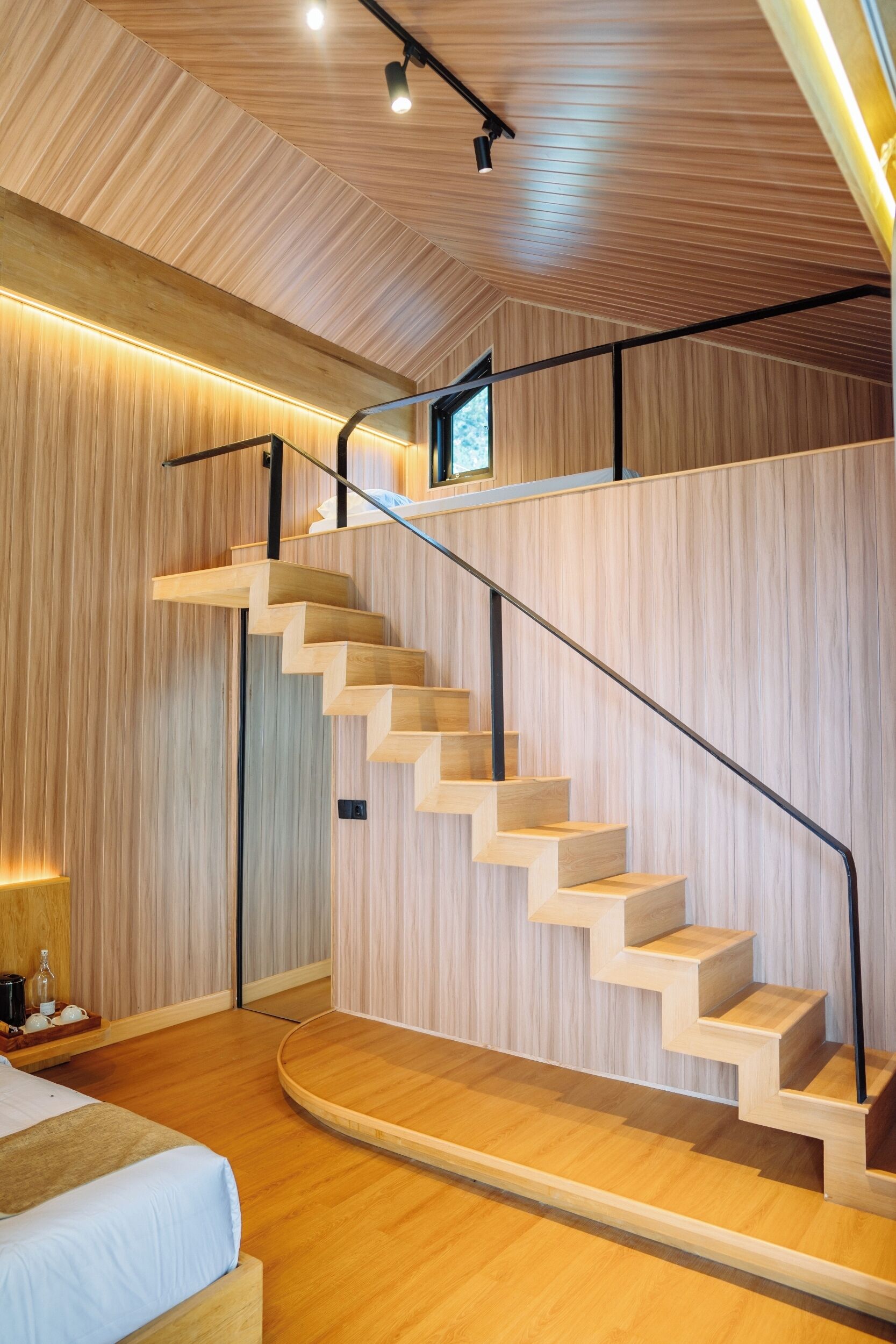 Een modern interieur met een houten trap, een bed en een klein tafeltje met flessen.