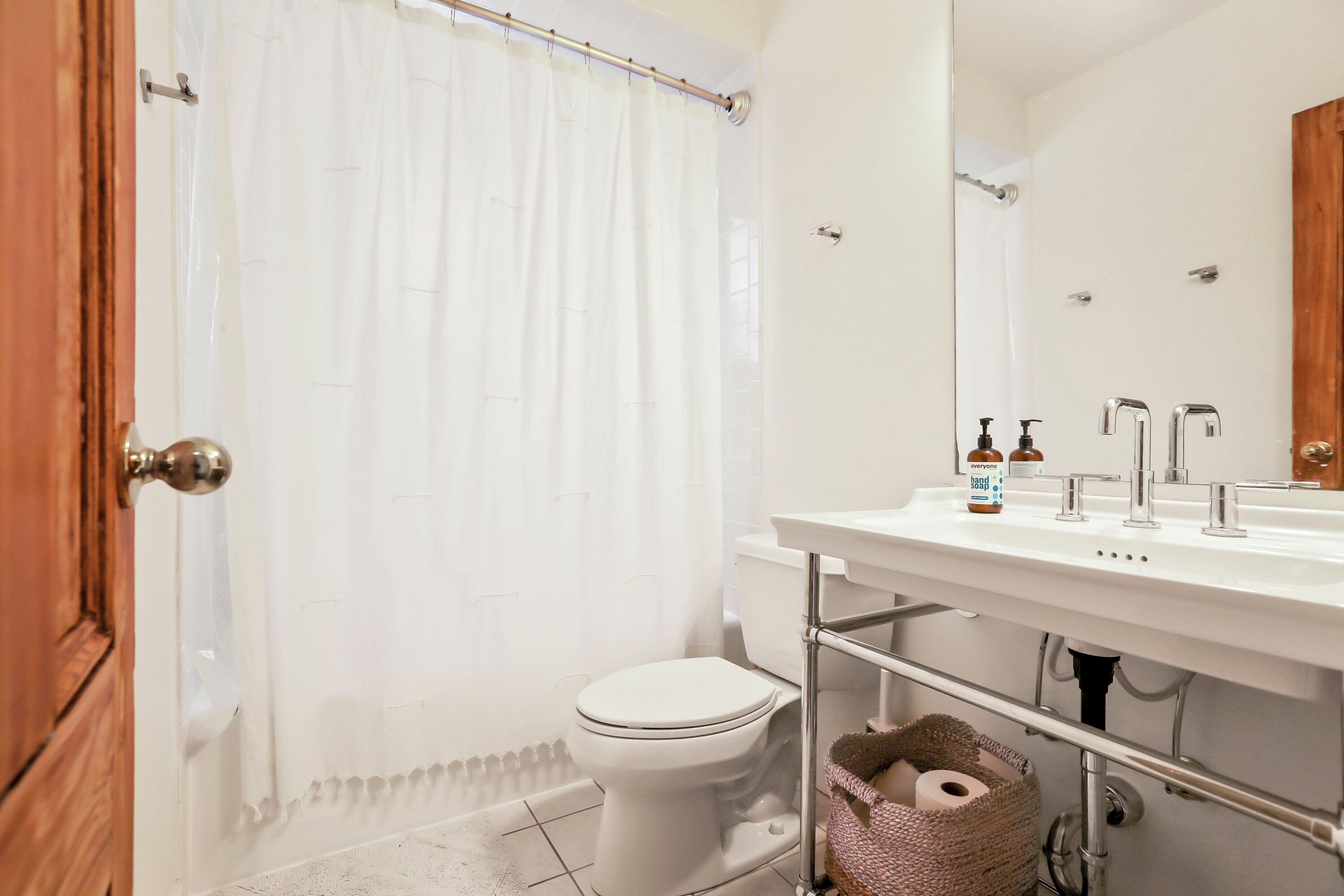 Ein Badezimmer mit Toilette, Duschvorhang, Waschbecken mit Spiegel und Toilettenartikeln auf dem Waschbecken.
