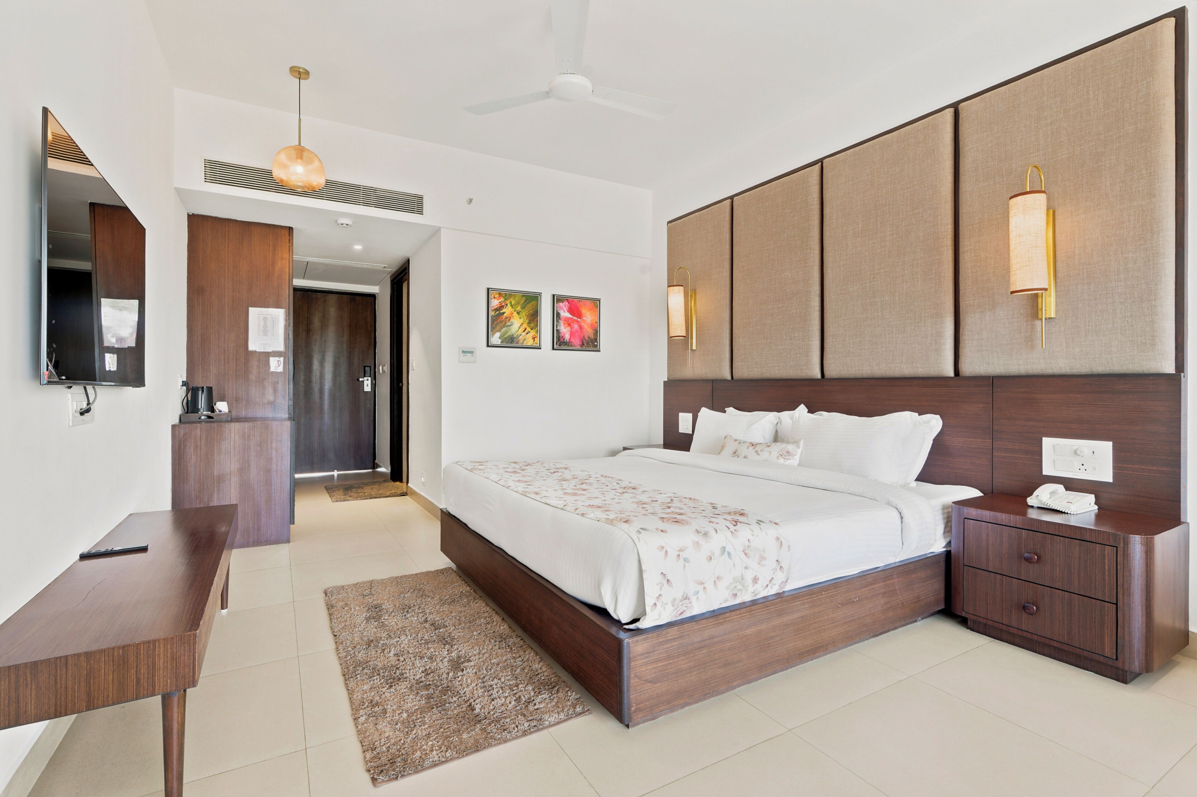 A modern hotel room with a large bed, bedside tables, a desk, and a mirror.