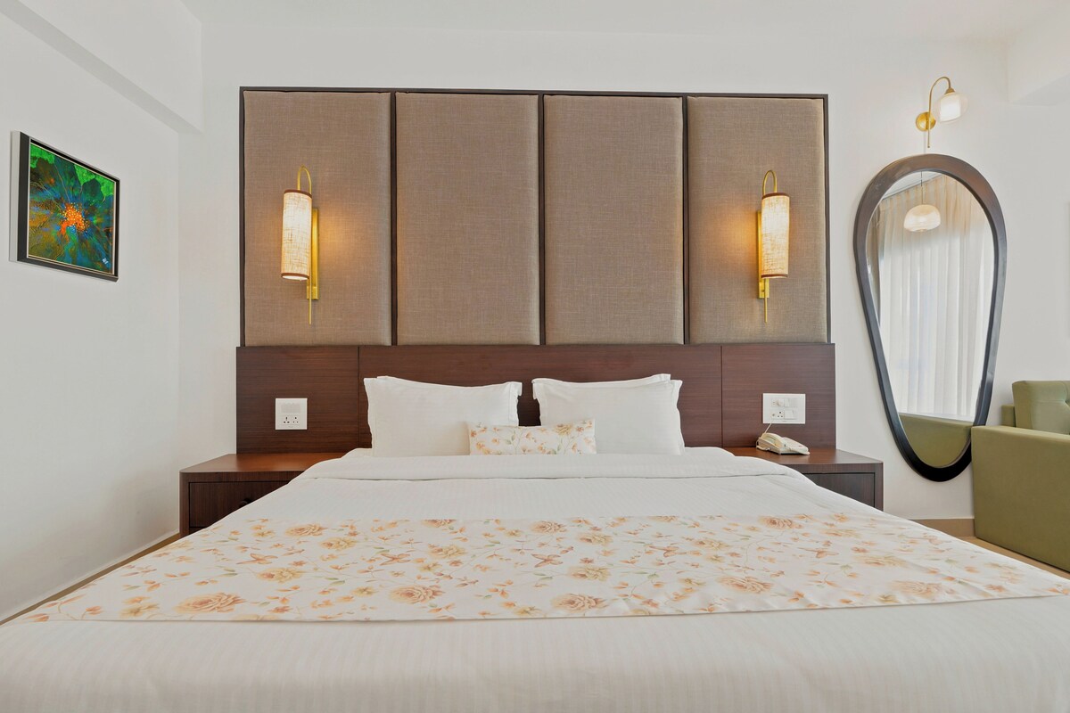 A hotel room with a large bed, two bedside tables, a wall-mounted mirror, and a painting on the wall.