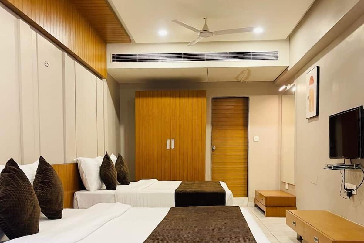 A hotel room with two beds, a wooden wardrobe, a television, and a ceiling fan.