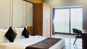 Habitación de hotel moderna con una cama grande, cabecera de madera, ventilador de techo y vistas al exterior a través de amplias ventanas.