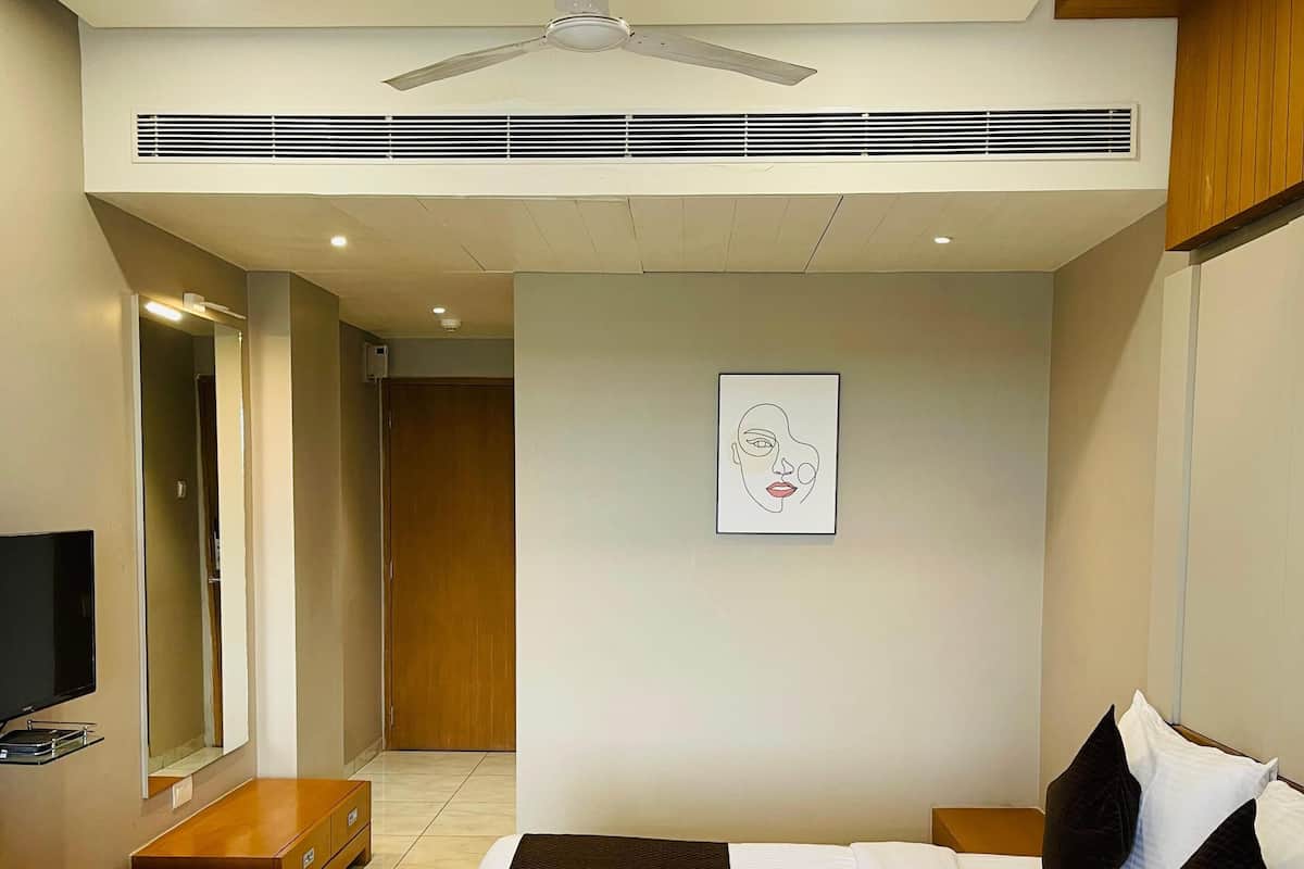 A modern hotel room with a bed, a TV, a ceiling fan, and a framed artwork on the wall.