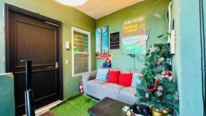 Une pièce chaleureuse avec un mur vert, une porte noire, un canapé gris agrémenté de coussins rouges, un petit sapin de Noël et une table sur laquelle sont posés des cadeaux.