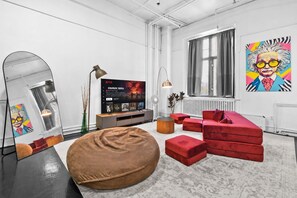 A modern living room with a large mirror, a red sofa, a brown bean bag, and a flat-screen TV displaying a Netflix show. - Cozy open concept Loft in the Heart of Old Port (Montréal)