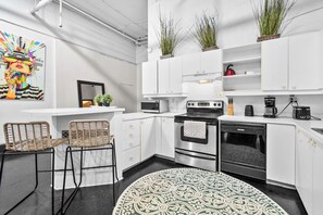 Una cocina moderna con armarios blancos, una estufa negra, un lavavajillas y una alfombra estampada.