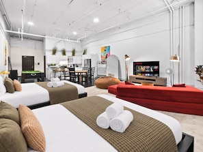 A modern hotel room with two beds, a red sofa, a dining area, and a TV displaying Netflix. - Cozy open concept Loft in the Heart of Old Port (Montréal)