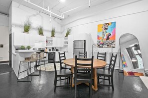 A modern kitchen with white cabinets, a central island, and a dining area with a round table and chairs. - Cozy open concept Loft in the Heart of Old Port (Montréal)