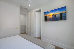 A bedroom with a bed, a painting of a sunset, and white doors. - Big Kahuna Steps to Beach w/ Waterslide Pool & Spa (Sarasota)
