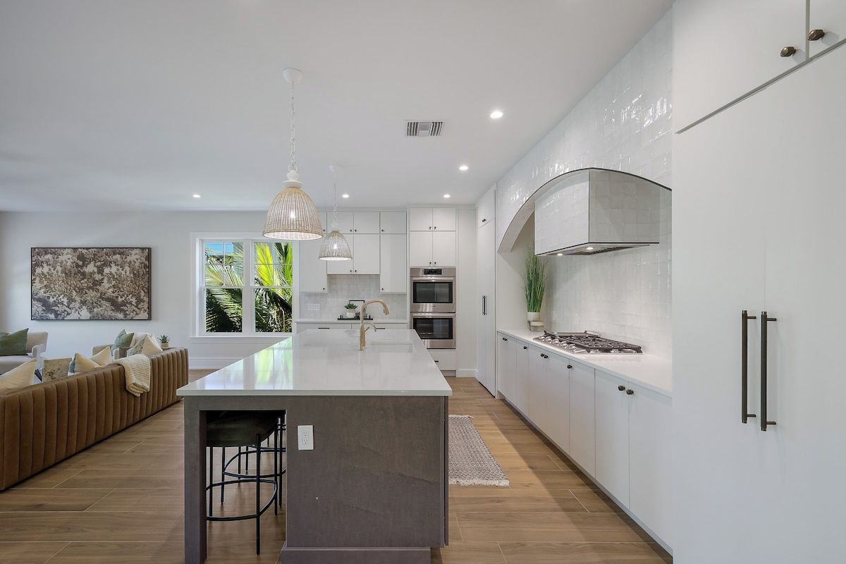 A modern kitchen with white cabinetry, stainless steel appliances, and a central island with stools.