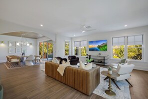 A spacious living room with a large TV, a sofa, and a dining area with chairs. - Big Kahuna Steps to Beach w/ Waterslide Pool & Spa (Sarasota)