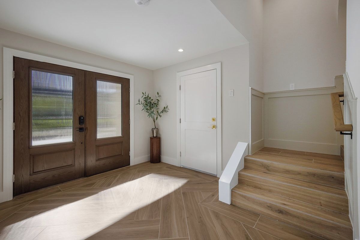 A spacious entryway with a wooden floor, a white door, and a staircase leading to an upper level.