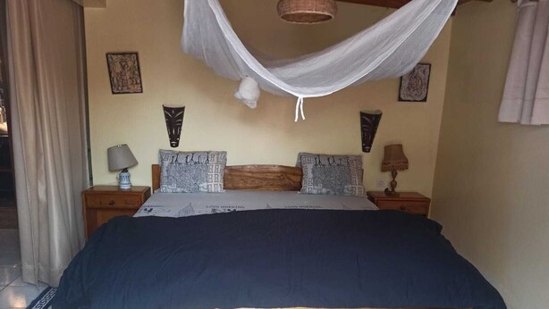 Ein Bett mit dunkelblauer Bettdecke, einem Holz-Kopfteil und zwei Nachttischen mit Lampen.