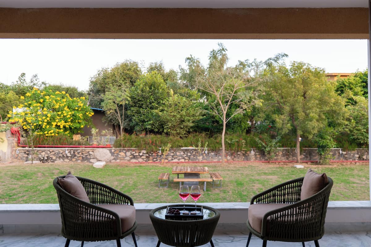 Une terrasse avec deux fauteuils en osier, une petite table et une vue sur un jardin agrémenté d’une table et de chaises en bois.