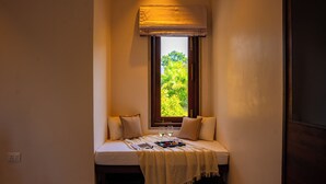Un cuarto acogedor con un banco incorporado, una ventana con vistas a la vegetación y una mesita de noche con una bandeja de frutas y vasos.
