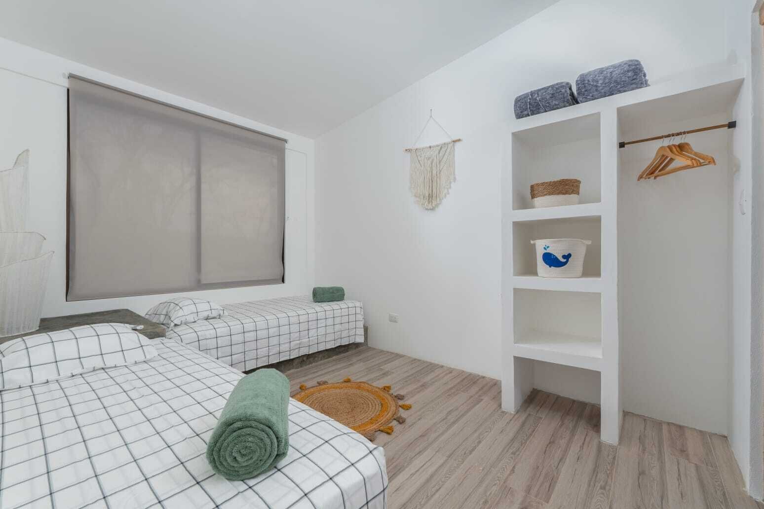 Une chambre avec deux lits, une armoire, une fenêtre avec un store et un petit tapis.