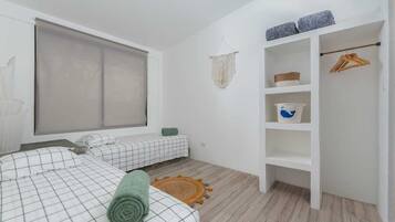 Une chambre avec deux lits, une armoire, une fenêtre avec un store et un petit tapis.
