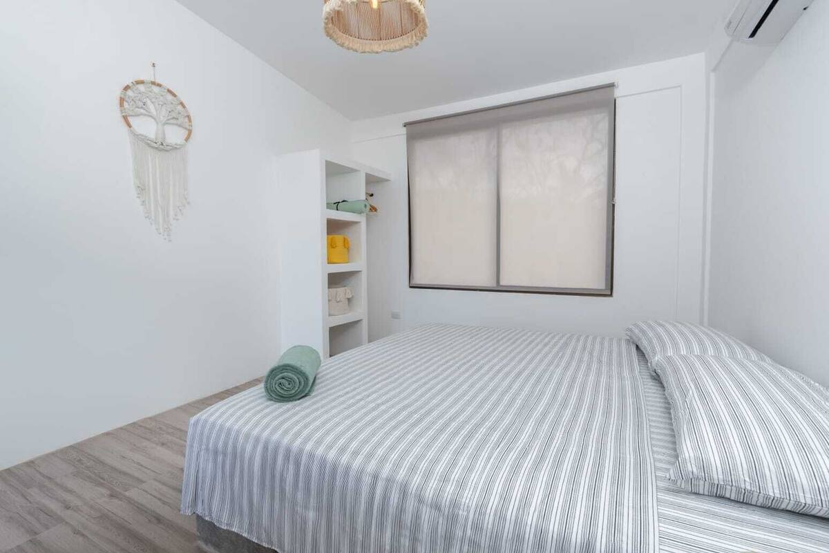 A bedroom with a bed, a wardrobe, a hanging macrame decoration, and a window with blinds.