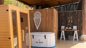 Egy fából készült kabin, üveg ajtóval, masszázságy, egy masszázsasztal, egy hűtőláda és egy falra szerelt álomfogó található benne.