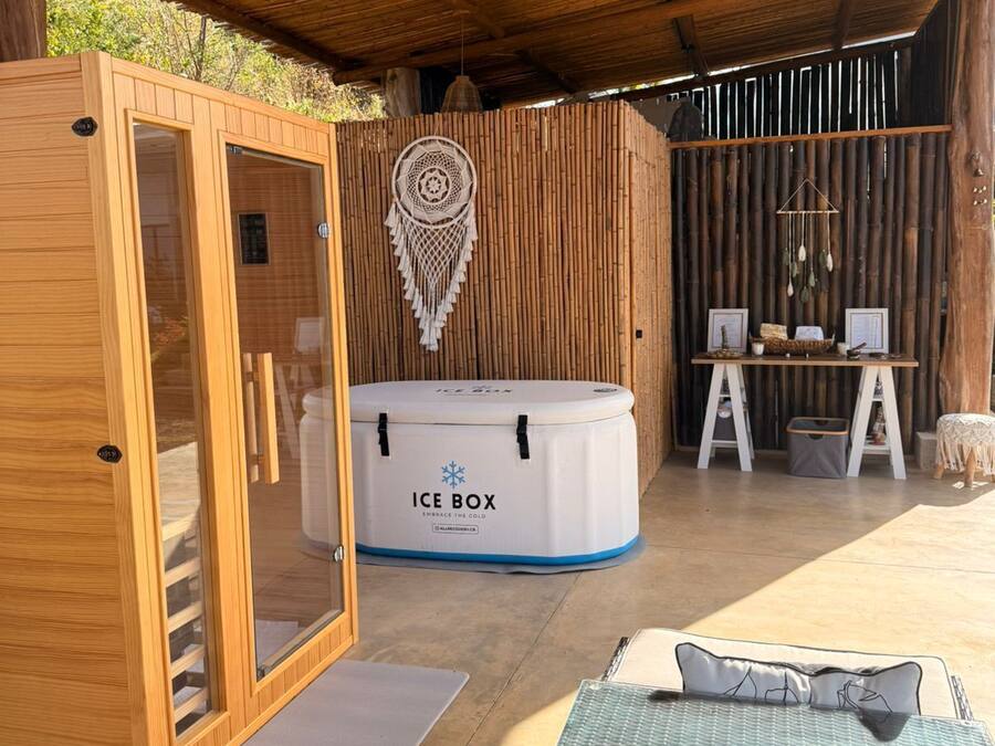 A wooden cabin with a glass door, a massage chair, a massage table, an ice box, and a wall-mounted dreamcatcher.