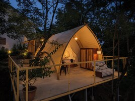 A tent with a wooden deck and a bed, surrounded by trees.