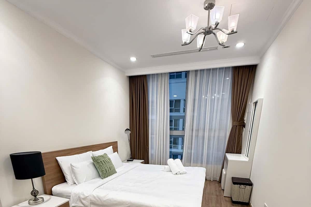 A modern hotel room with a large bed, bedside tables, a ceiling fan, and a window with curtains.