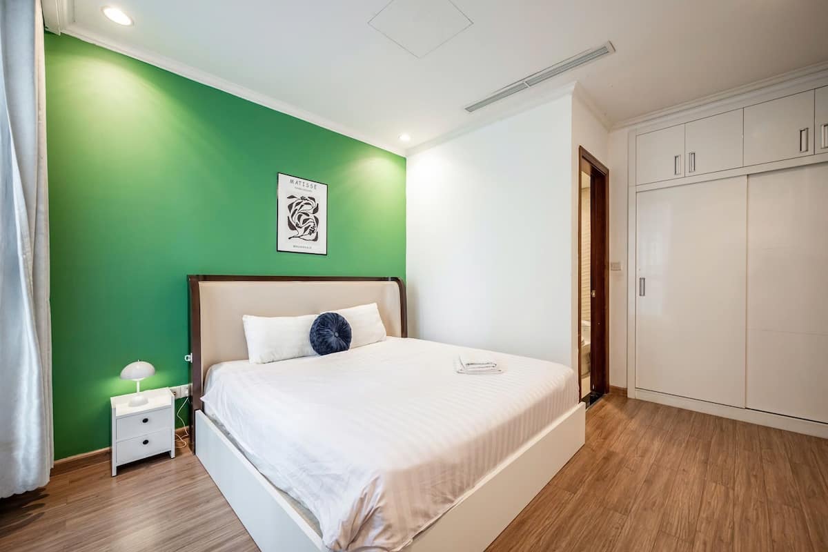A bedroom with a green accent wall, a bed with white bedding, a nightstand with a lamp, and a wardrobe.
