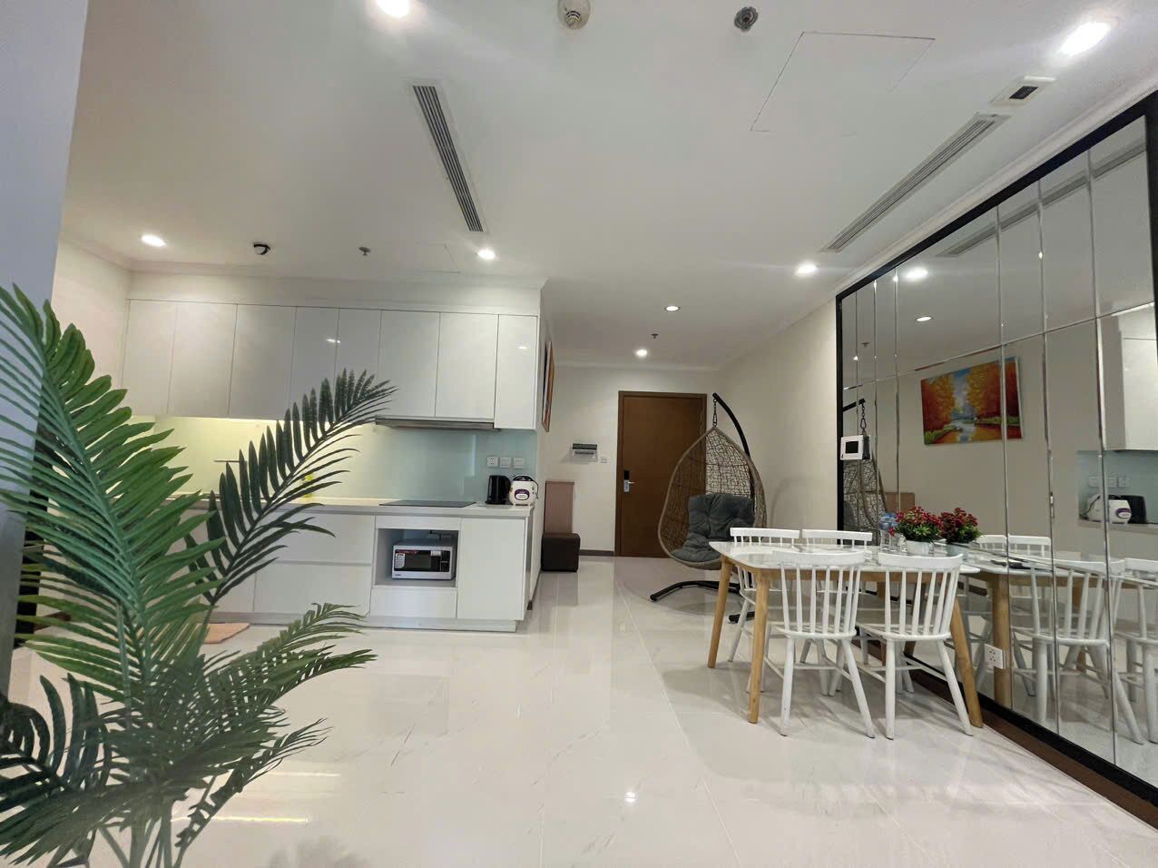 A modern kitchen with white cabinets, a dining area with a white table and chairs, and a hanging chair.