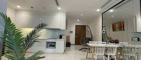 A modern kitchen with white cabinets, a dining area with a white table and chairs, and a hanging chair.