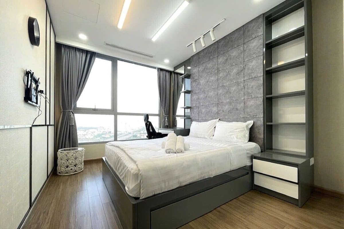 A modern bedroom with a large bed, a bedside table, a wardrobe, and a window with curtains.