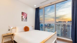 A modern hotel room with a large bed, a nightstand, a bedside lamp, a city view through large windows, and a framed floral artwork on the wall. - Saigon Stay at Vinhomes Central Park (Ho Chi Minh City)