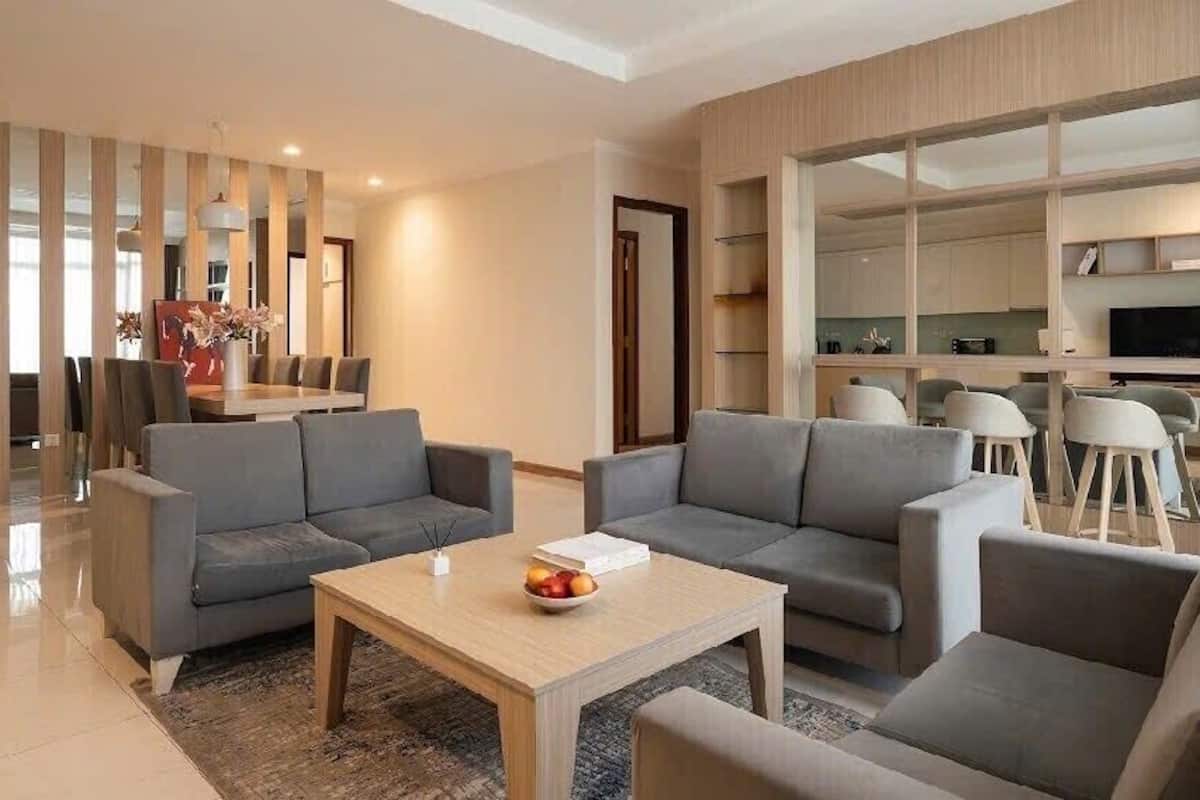 A modern living room with grey sofas, a wooden coffee table, and a dining area with a large table and chairs.