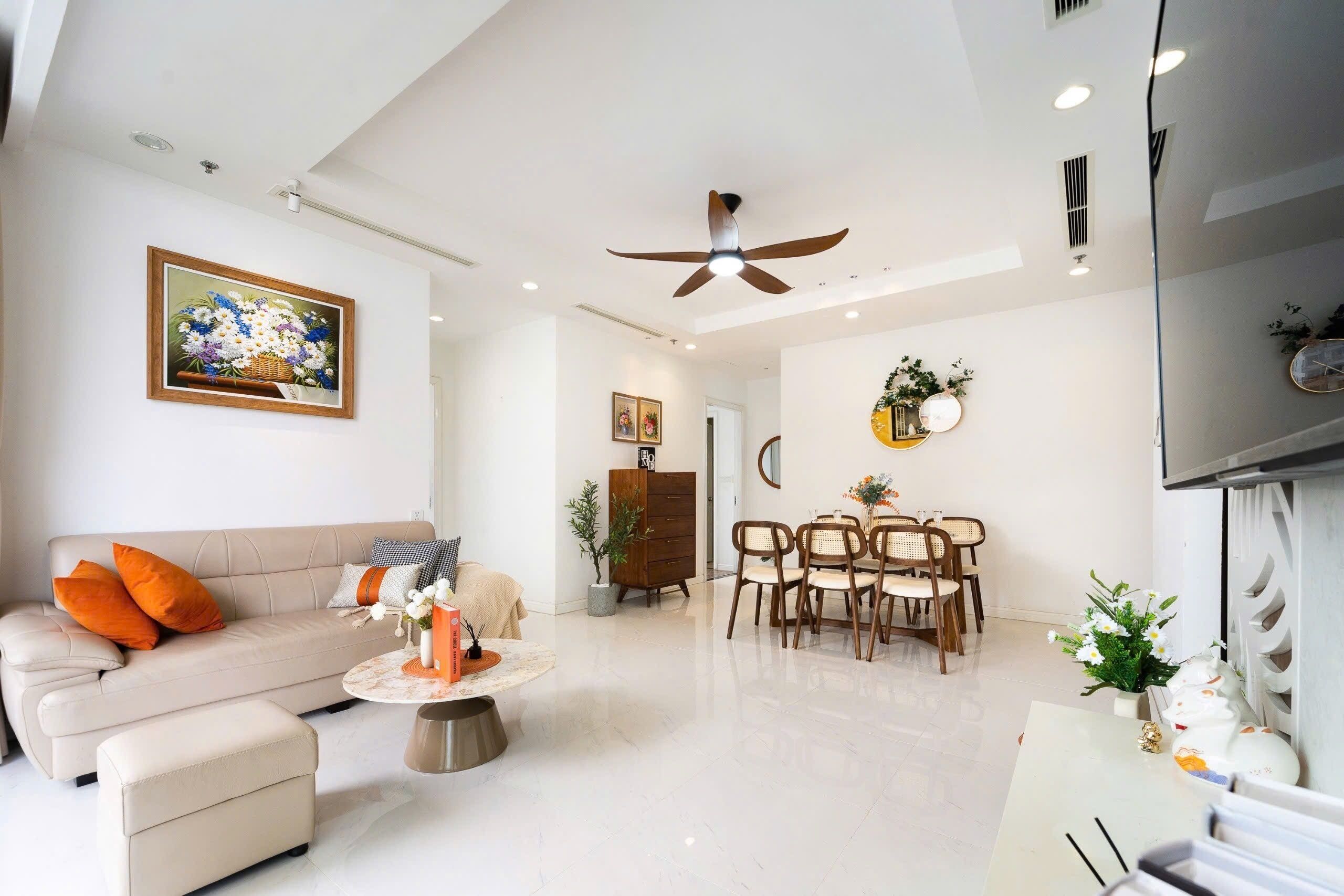 Una sala de estar moderna con sofá, reposapiés, mesa de comedor, sillas, ventilador de techo y obras de arte en la pared.