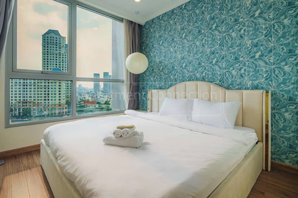 A hotel room with a large bed, a view of the city through a window, and a patterned wall.