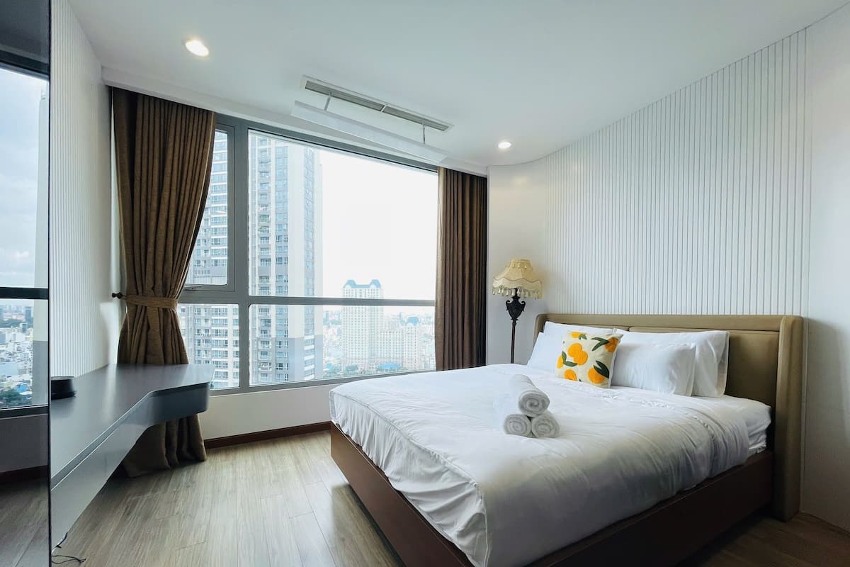 A modern hotel room with a large bed, a desk, and a view of the cityscape.