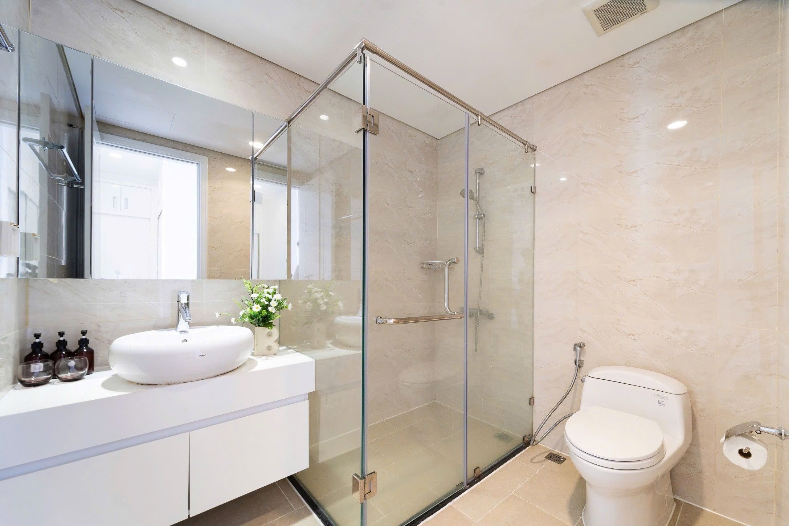 A modern bathroom with a glass-enclosed shower, a white sink, and a toilet.