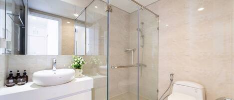A modern bathroom with a glass-enclosed shower, a white sink, and a toilet.